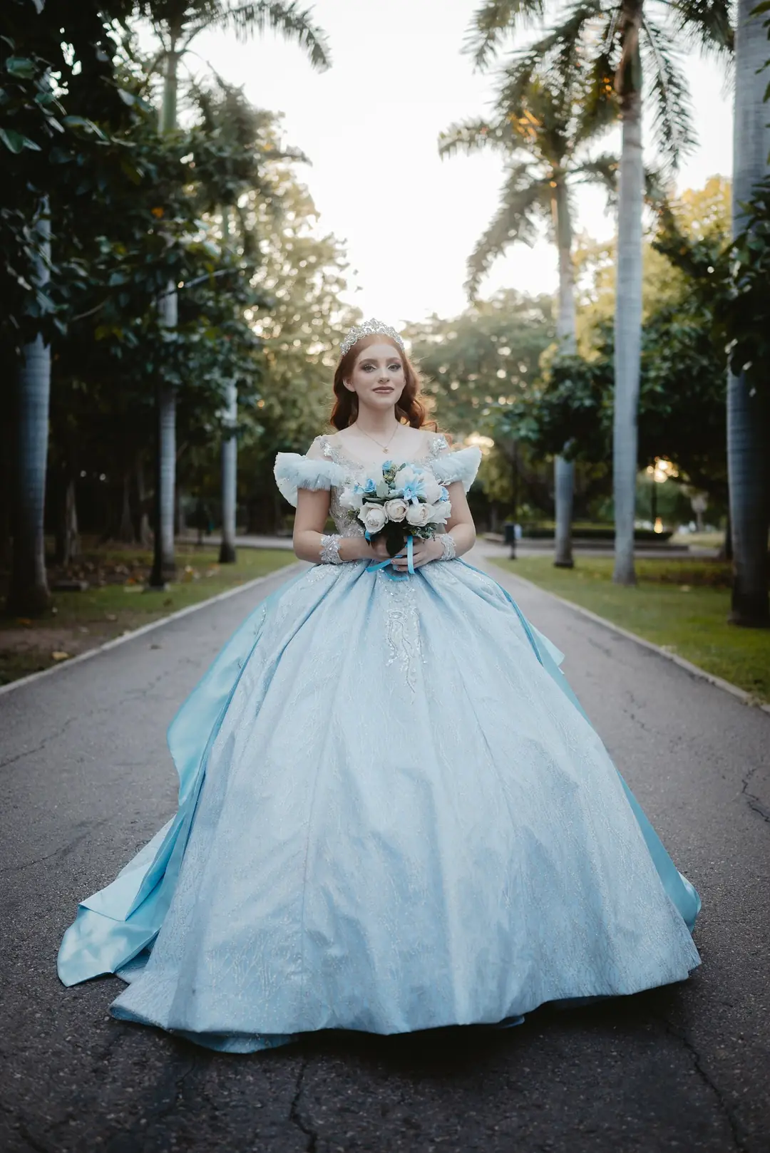 Una quinceañera de vestido celeste en una avenida de palmeras